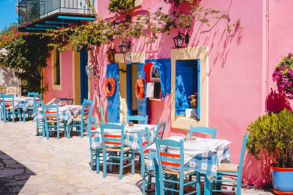 Traditional greek vivid lilac colored tavern on the narrow Mediterranean street on hot summer day.