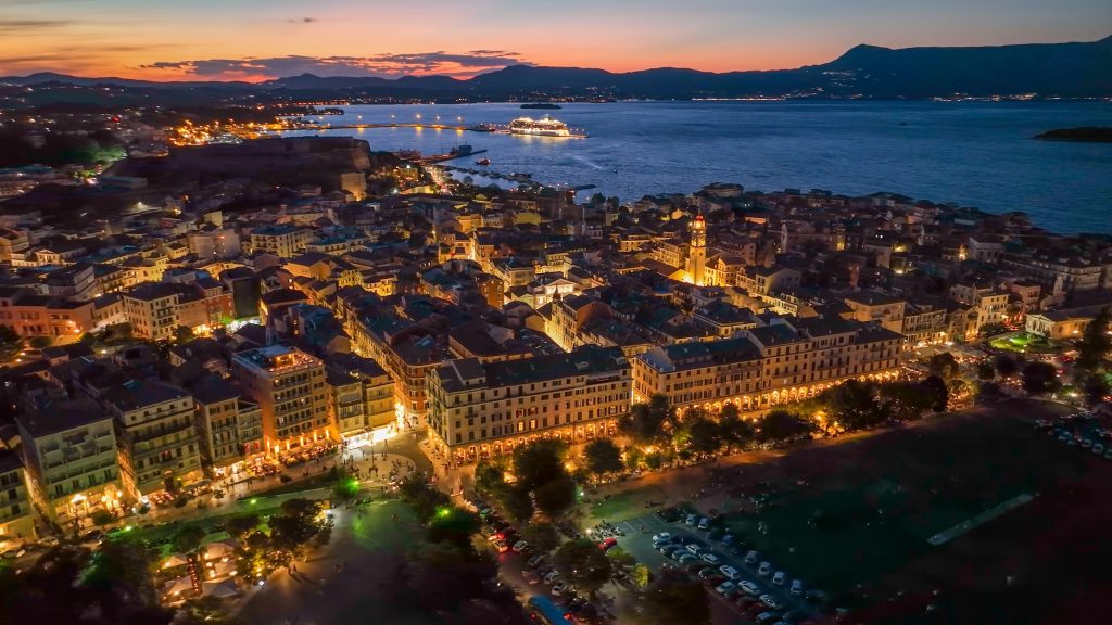 Old town with illumination against background of red sunset sky in Kerkyra, Corfu island. Evening aerial sunset view of Kerkyra, capital of Corfu island, Greece. 4K HDR shot 2 SSUCv3H4sIAAAAAAAACnSSTW/CMAyG75P2H1DOINqGdrDjzvuQtiPiYBIXIkKCkrTThPjvcxrKMmm71a+dx/Zbn+/vJhO2Ba8Ee5ycY0Sx0rrzwUFQ1pBcTK+6QyPR5UrveFPkAqg8QqmCdQp0Lm4hiL2BI5JoOq2jfBmSzAcInUcfZ7lKAgLuiJHEGyINvE7xZEwMSXpBKfbUKS2V2fn5Mxh5BHfwbJqV+W4by16UF6g1GLSdZ2M+Nf+H/EpDOvwL9oEwfxMIZv6uenLqhksfm5tLOzTi62ehyHZIfvcYB8WQ70bJ8kbapI8BeHXIoUZIpq1TB3b4DOiOuY3QSWUzB3srQMcCnpFAncDBr3cnpwSZmCk27IcbGEnCdia4uAxbLkZTmLb2BFsd/3FLjXDU9+A9PZCjnnUXdHP2mHUyNgxbsURlkk4hhiXnvC6KVcGritdV09TXgnQ+e0WcYaARRLE4KJnvpeIErJVY1tWDnK34sp0tJOBs1TyIGRS8KUW5aItKkPWXbwAAAP//AwBT2Gs7JwMAAA==